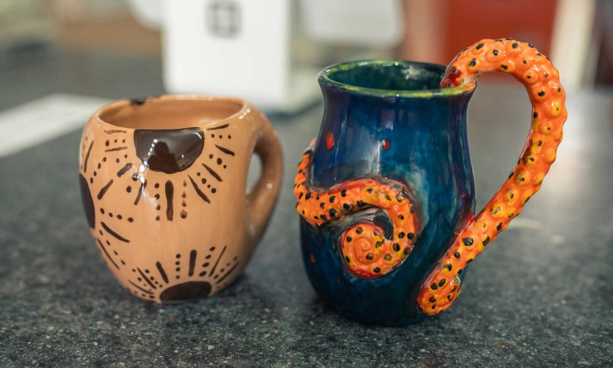 Two hand-painted mugs sit on a flecked black and gray counter.