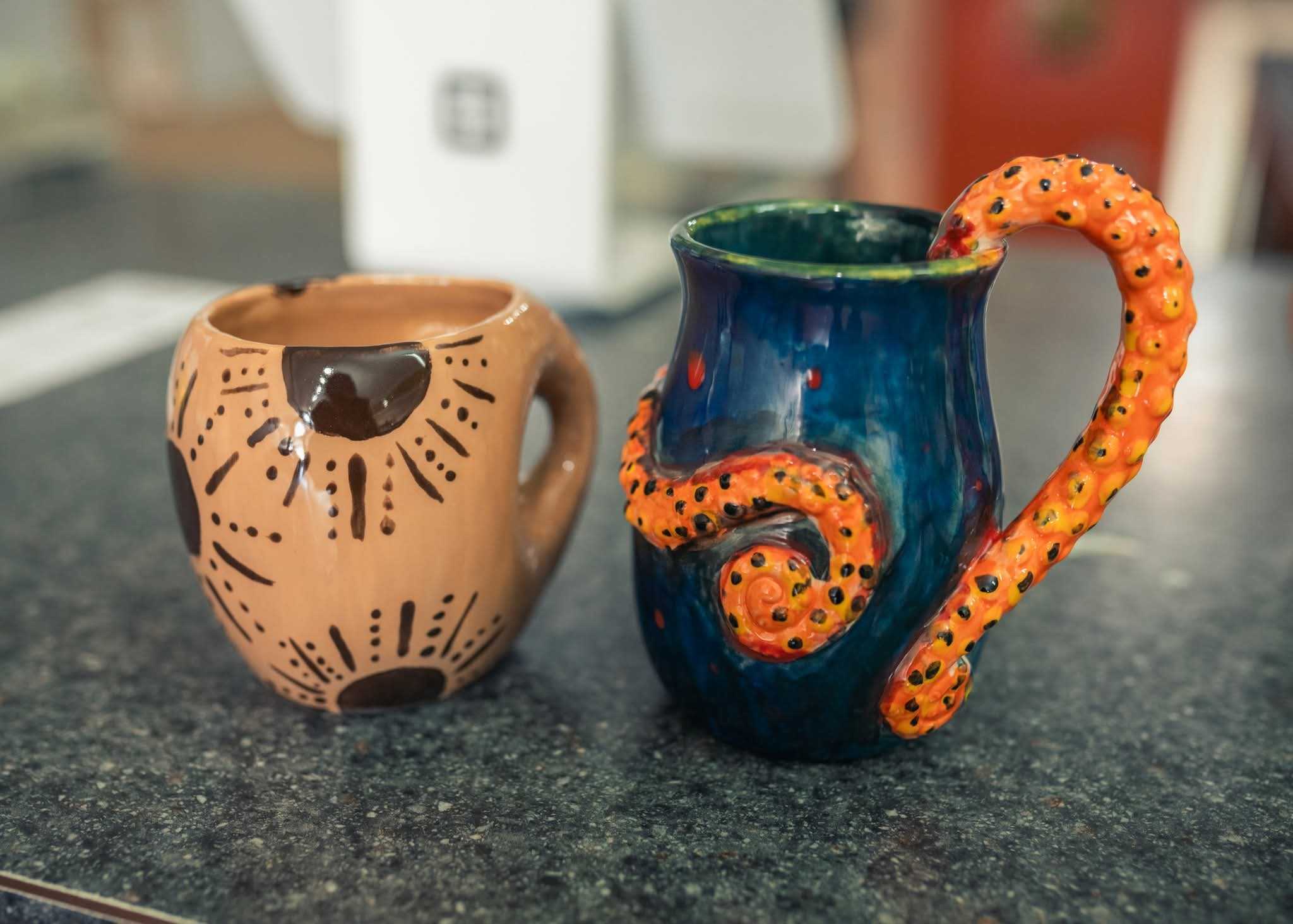 Two hand-painted mugs sit on a flecked black and gray counter.