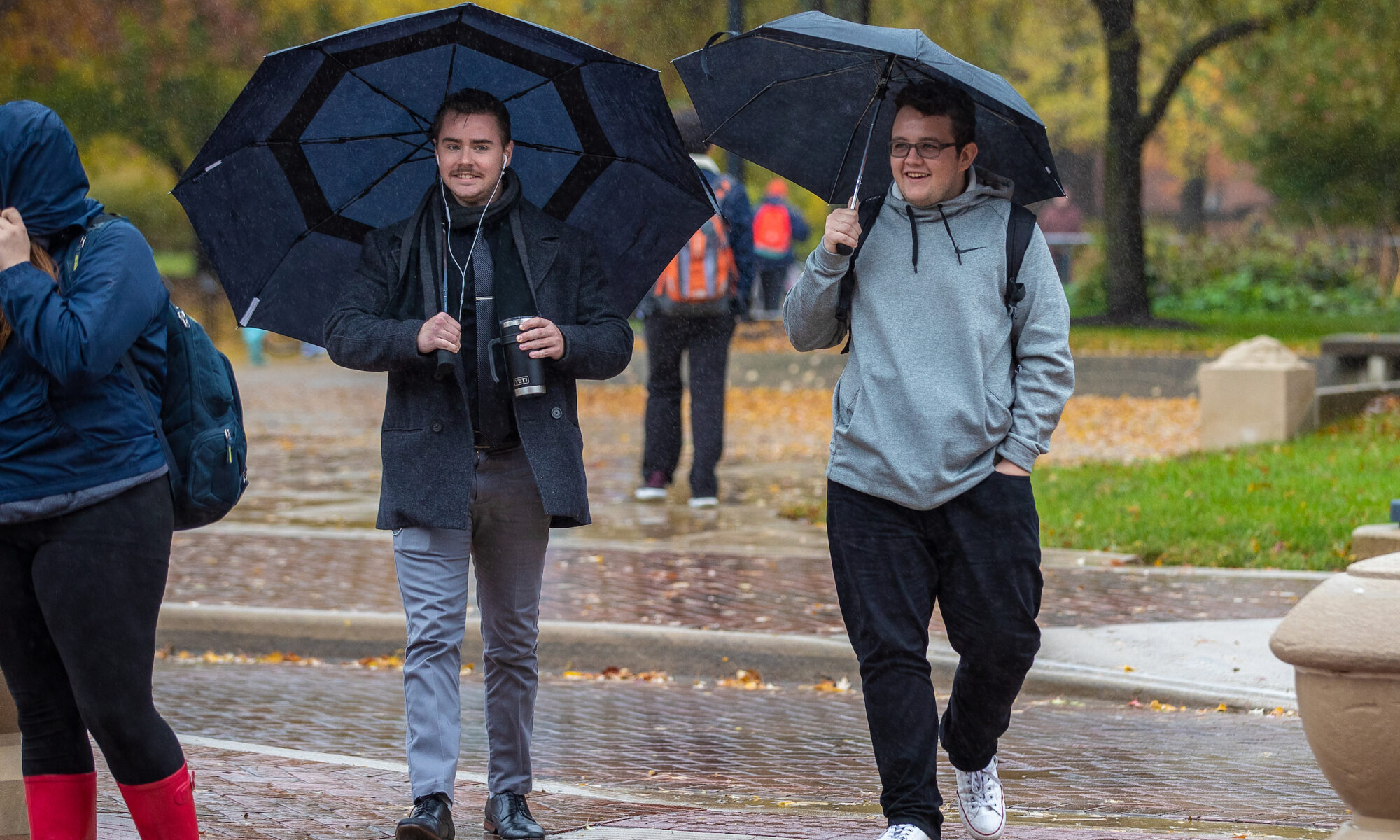 people holding umbrellas walk down a rainy campus sidewalk