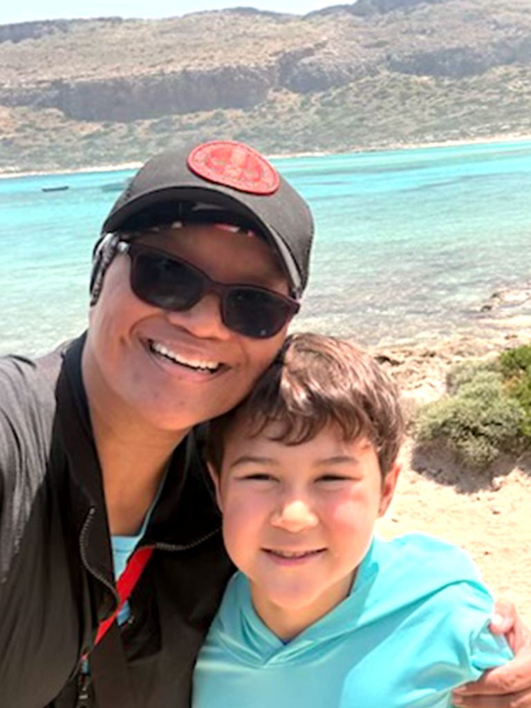 A smiling woman and child taking a selfie against a beautiful beach backdrop