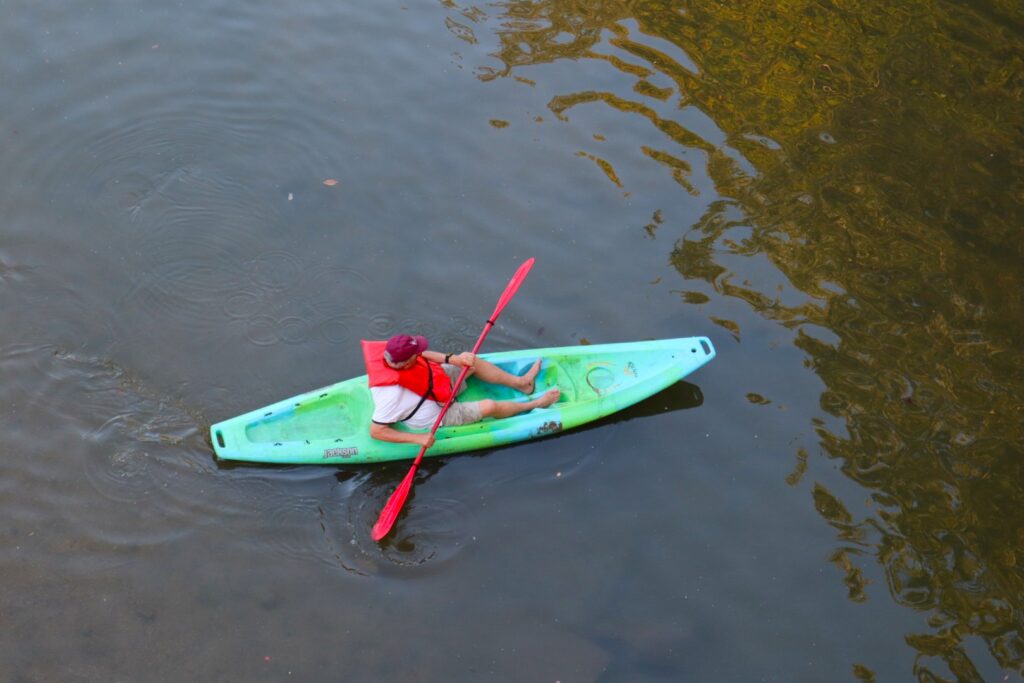 A photo taken from above of a person in a red life vest in a green kayak on the river. 