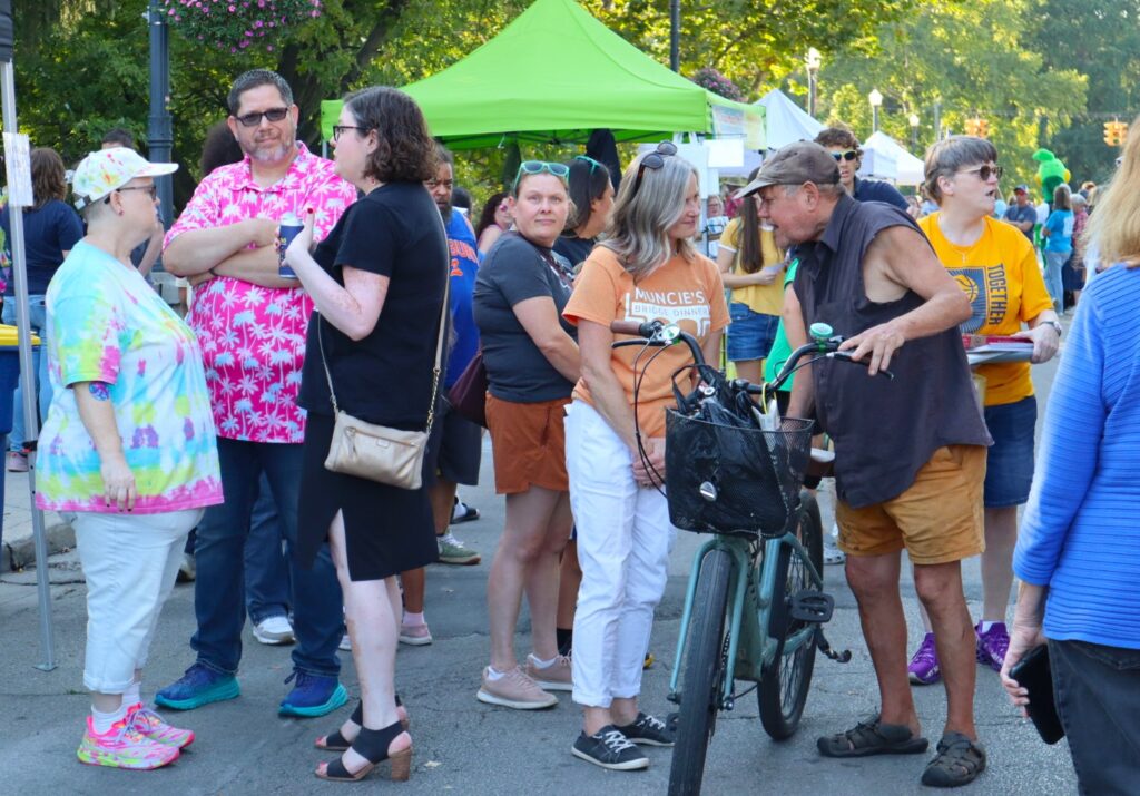 A crowded view of the bridge with a bright green vendor's tent rising up in the background. A man with a bicycle stands a little in front of the crowd looking down at it like he is about to ride it.
