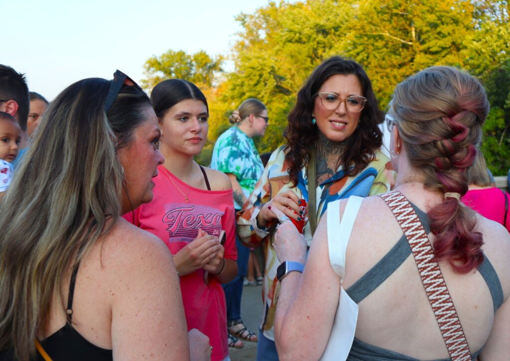 A group of woman chat on the bridge while the crowd mills behind them.