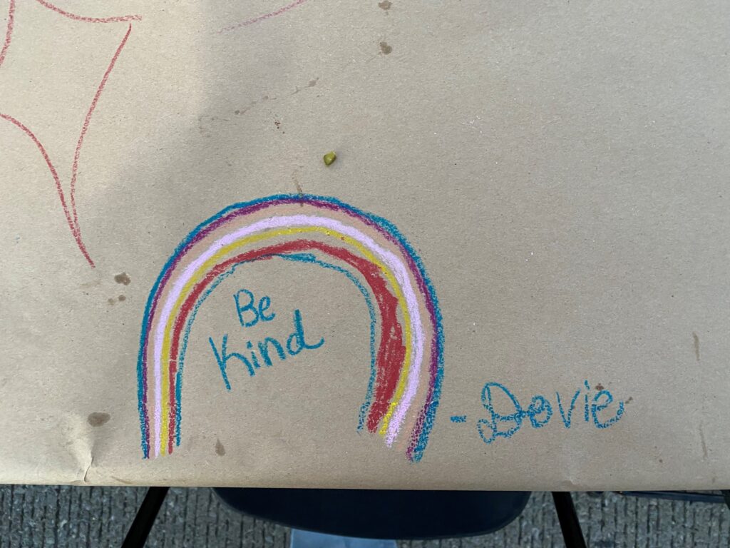 A beige paper with a drawing of a rainbow on it. Under the rainbow are the words "be kind" and to the right of the rainbow it says "-smile"