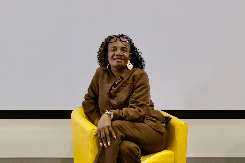 2026 CenterPoint Scholar Kim Hampton sits with her legs crossed at the knee, smiling at the camera from a yellow arm chair