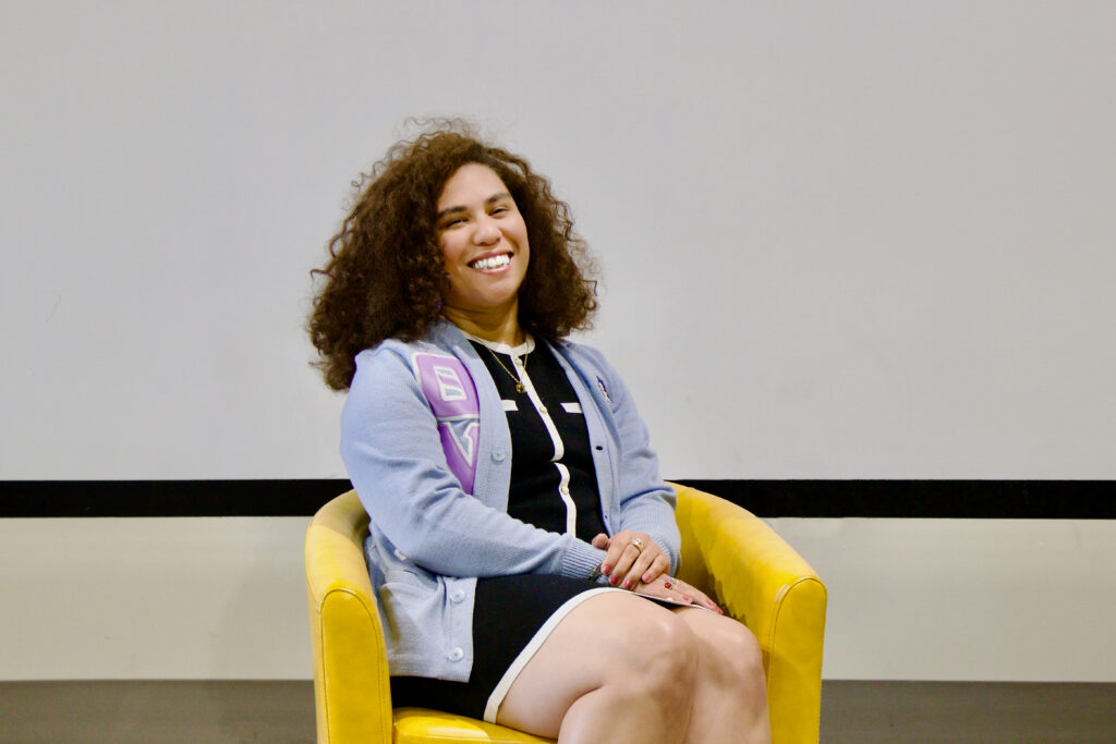 Monique Vargas, one of the 2026 CenterPoint Scholars sits smiling in a yellow chair against a white wall.