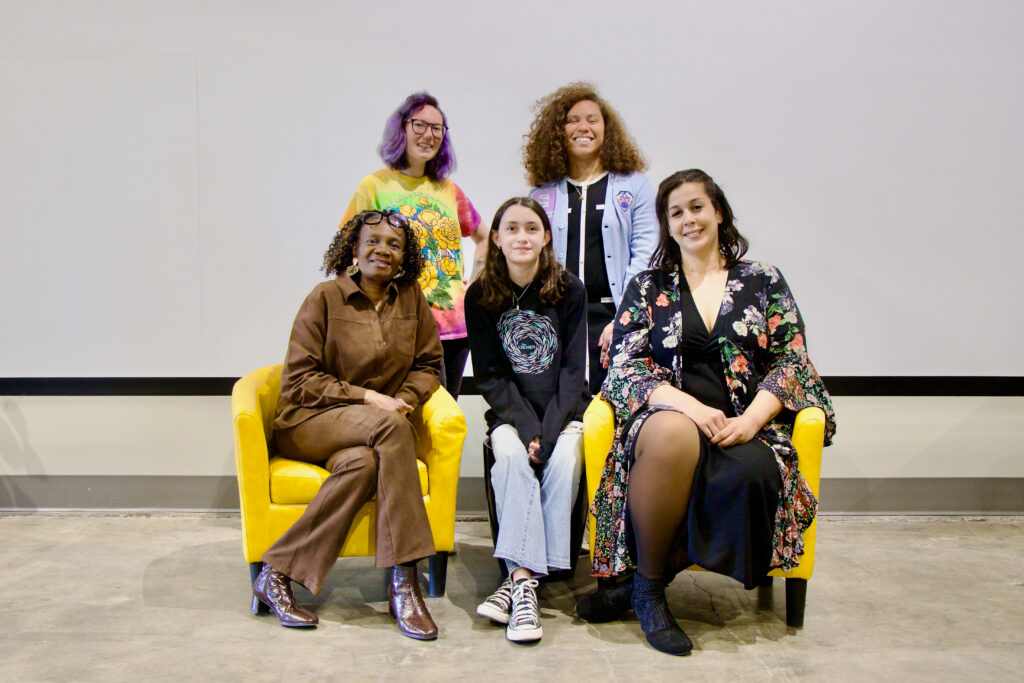 Group photo of the 2026 CenterPoint Scholars, five women in a white room with black trim and beige floors. Two stand in the back, and three sit in front of them in yellow arm chairs.
