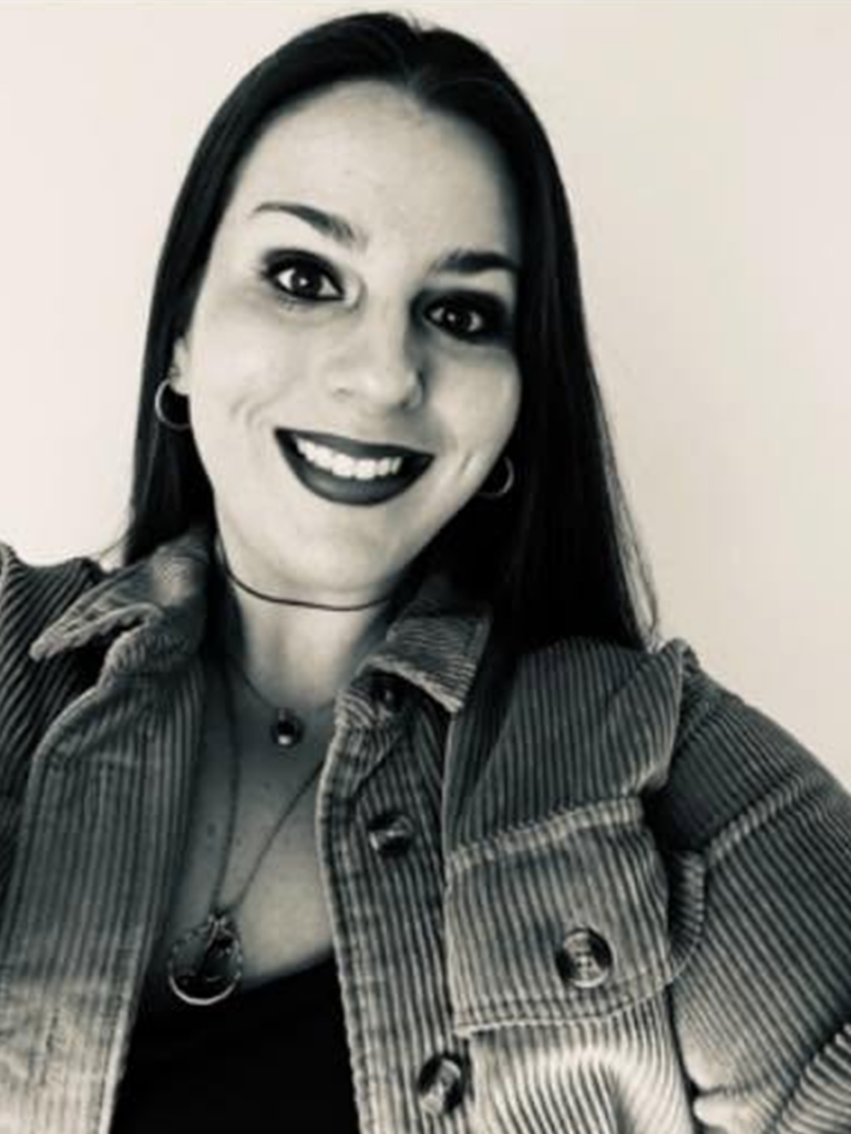 A black and white image of Lauren Prazeau against a white backdrop. She is smiling and wearing a denim jacket over a black shirt.